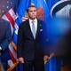 Color photograph of Attorney General Todd Blanche standing in a suit in front of American flags and next to a White House seal, between two Trump officials.